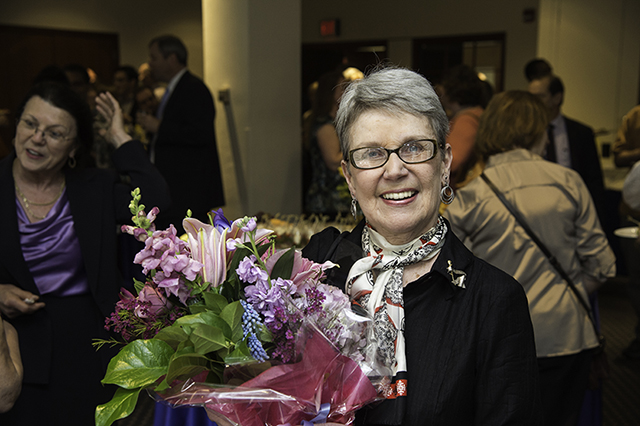 Suzanne O'Brien smiling at the camera while holding a bouquet of flowers with a room full of people in the background.