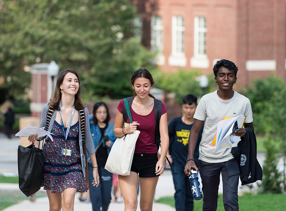 Photo of students with backpacks and papers walking on campus