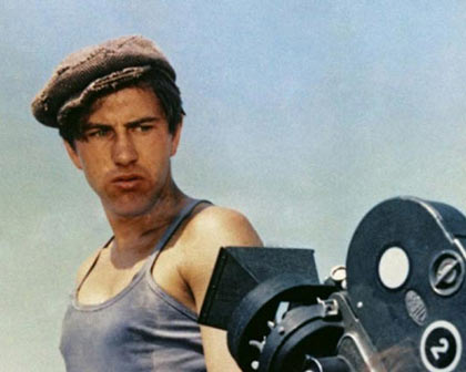 man in a newsboy cap staring at a 1930s film camera