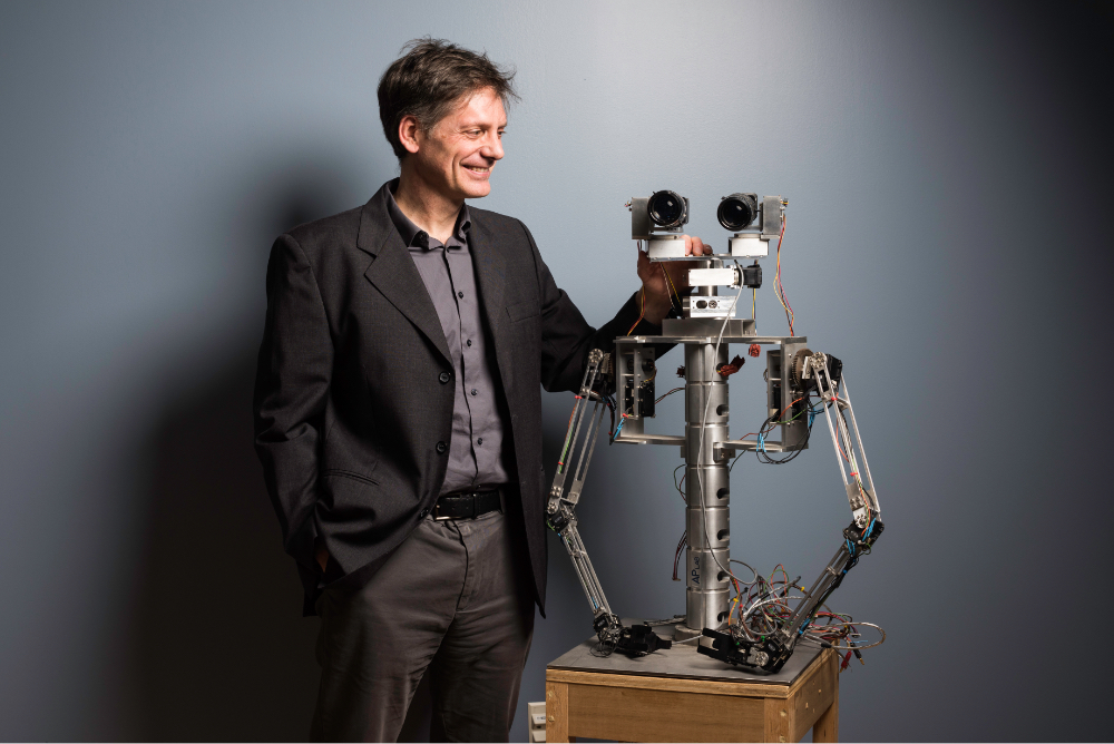 Faculty robotics researcher standing next to robot head and upper torso at University of Rochester