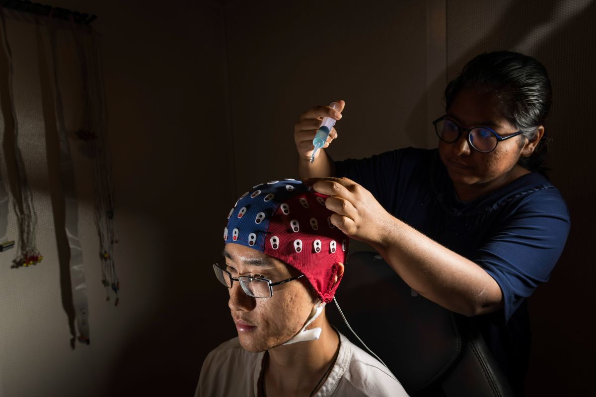 Senior biomedical engineering student Sophea Urbi Biswas adjusts an electroencephalography cap on fellow lab member Jin Dou, a biomedical engineering PhD student.