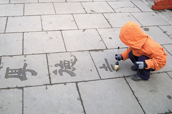 A child writing characters on a sidewalk.
