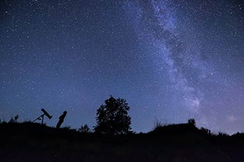 A person in silhouette viewing stars in the night sky.