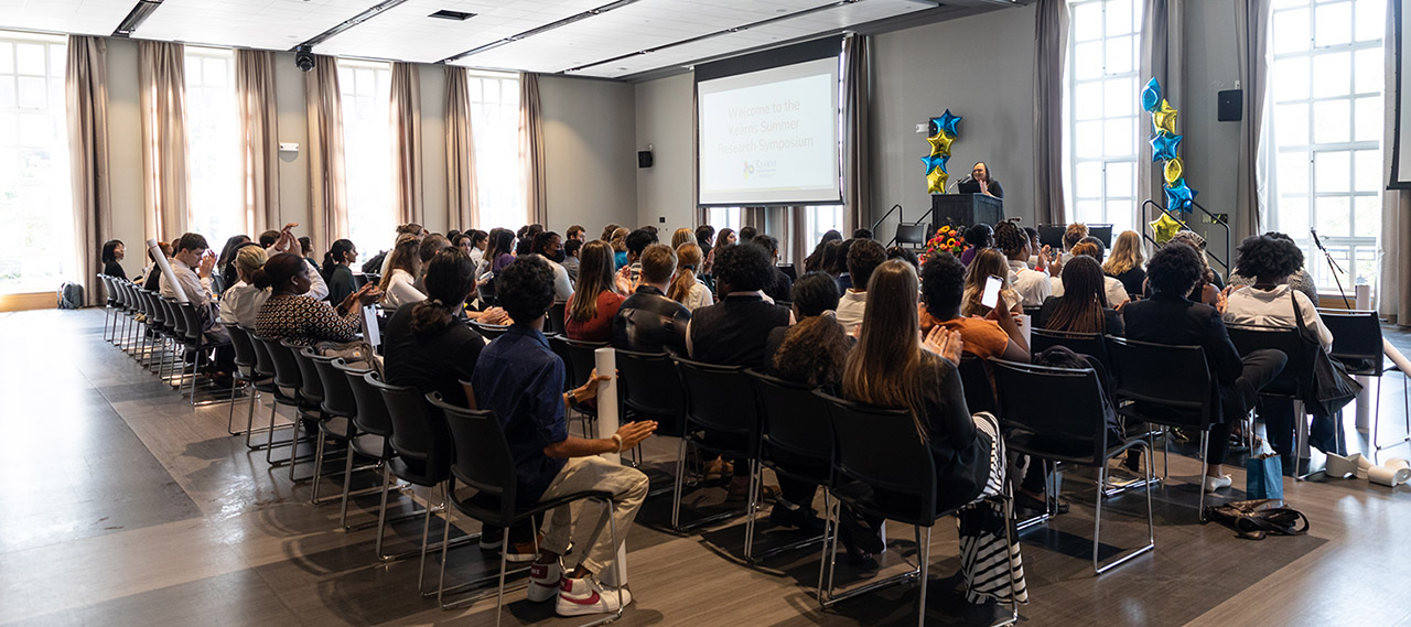 Students sitting in an audience and listening to a presenter at a symposium.