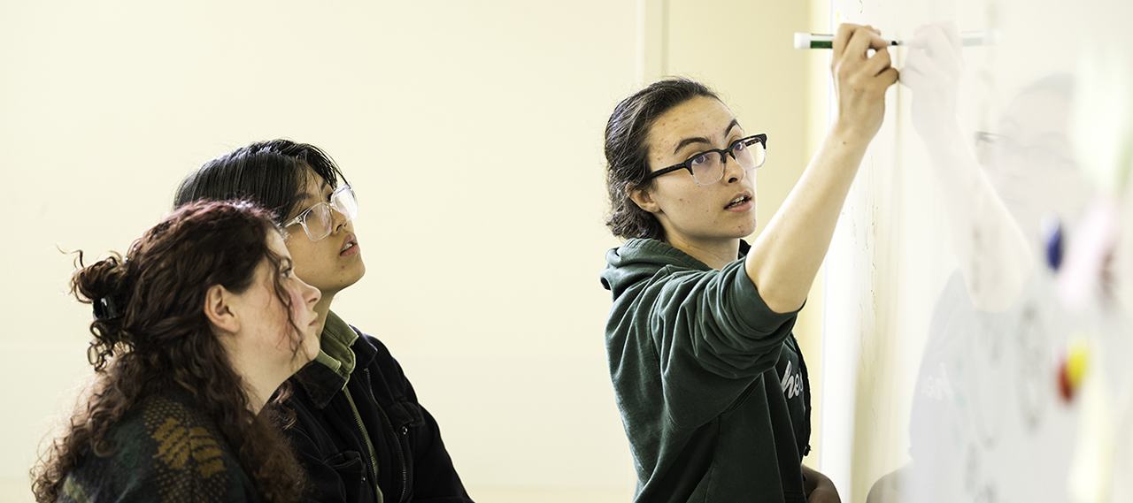 Three students working on a white board.