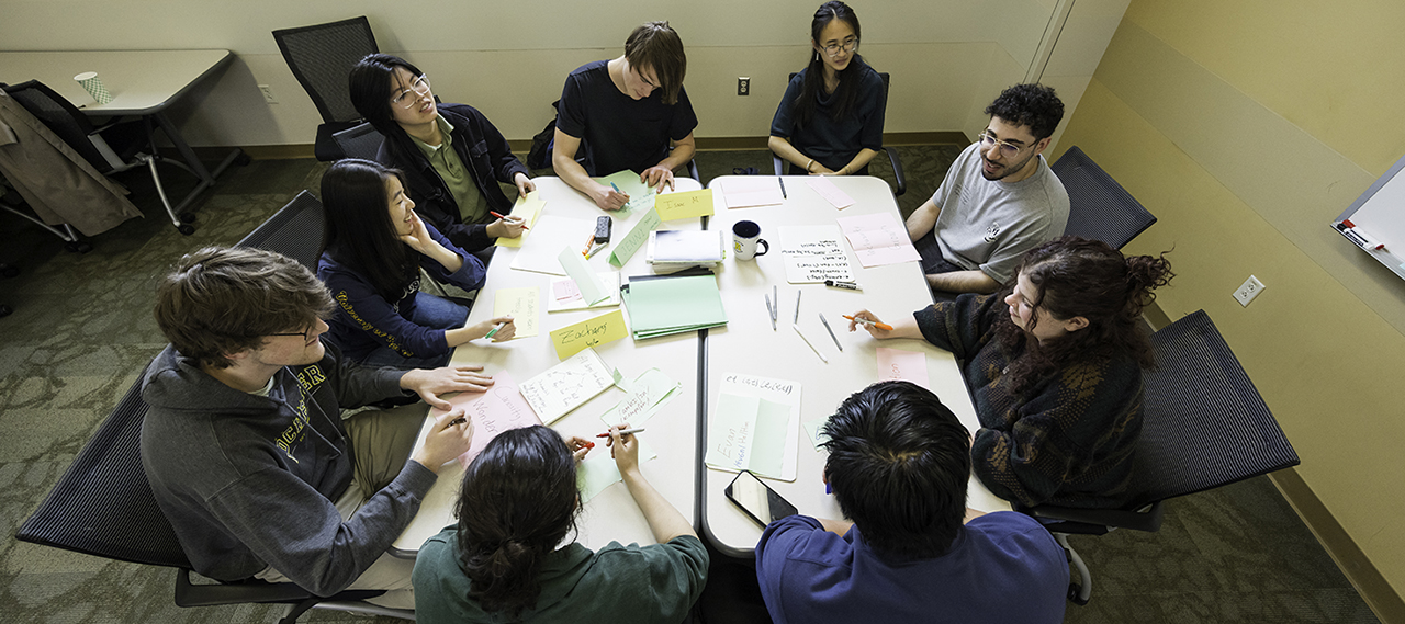 A group of students working around a table covered in documents.