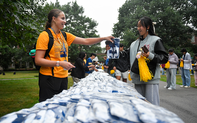 An orientation student staff member hands a jersey to a new student on Eastman Quad