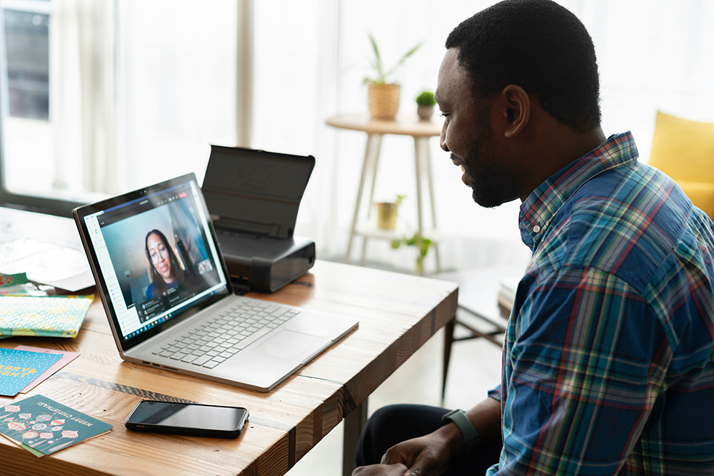 A man in a plaid shirt video chats with a woman on a tablet while sitting in a chair 