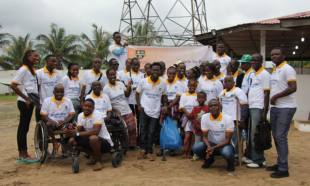 Two students gathered with a group of people all wearing Projects for Peace t-shirts.