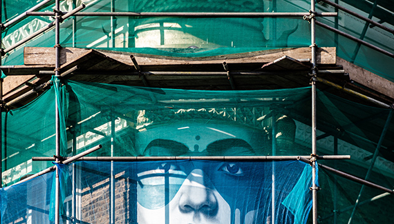 mural face visible behind scaffolding on building