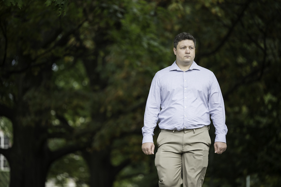 Man in khaki pants and blue shirt walks across University quad