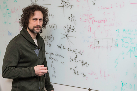 Andrew White writes equations on a whiteboard.