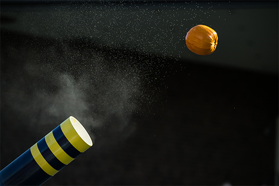 A pumpkin launches through the air just after being fired from a blue and yellow cannon.