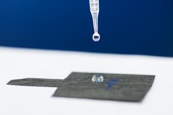 Dropper deposits a drop of solution onto a grey paper
