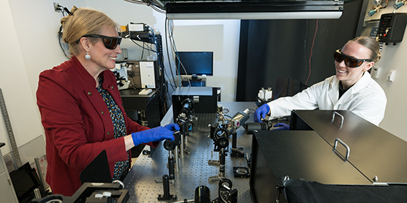 Astrid Muller and Madeleine Wilsey adjust mirrors and lasers on an optical bench.
