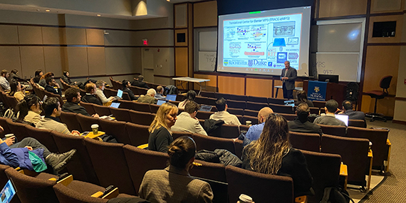 Jim McGrath presents a slide about TraCe-bMPS in front of a filled auditorium.
