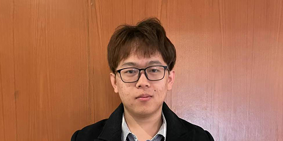 Andy Liu stands in front of a wooden background.