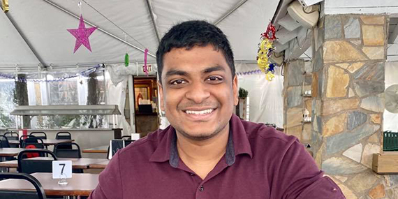 Michael Chavrimootoo sits at a table smiling.