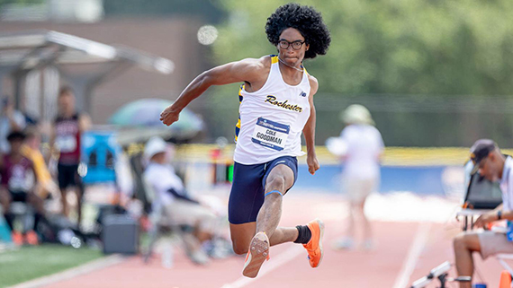 Cole Goodman performs the triple jump on a track while spectators look on.