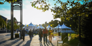 people walking towards white tents with yellow and blue balloons during sunset