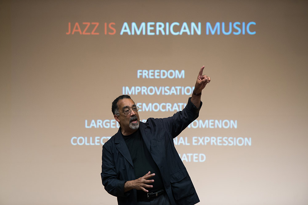 Paul Burgett teaching History of Jazz, standing in front of a classroom screen that reads JAZZ IS AMERICAN MUSIC