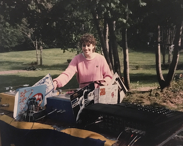 yearbook photo of Jacqueline Volin behind a large soundboard and records in a park setting with trees in the background