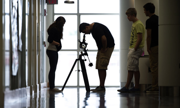 students in a backlit hallway, one of them looking into a telescope