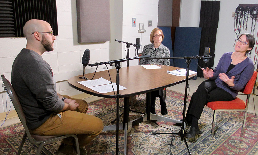 three people sitting around a table with microphones for a radio interview