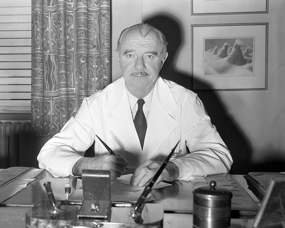 black and white photo of a man in a lab coat sitting at a desk