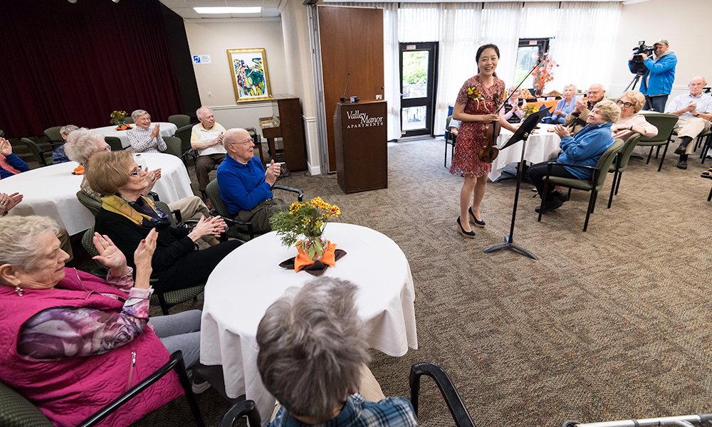 violinist bows before a crowd of senior citizens clapping