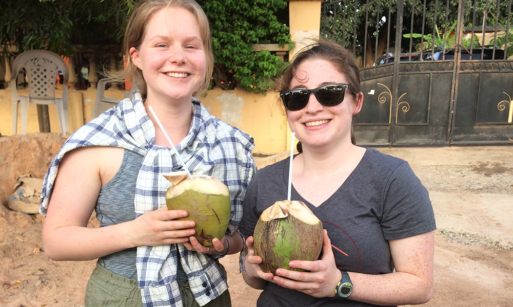 two students smiling, drinking from coconuts with straws
