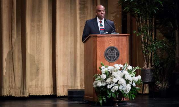 Lee Koonce speaking from a podium on stage at Strong Auditorium