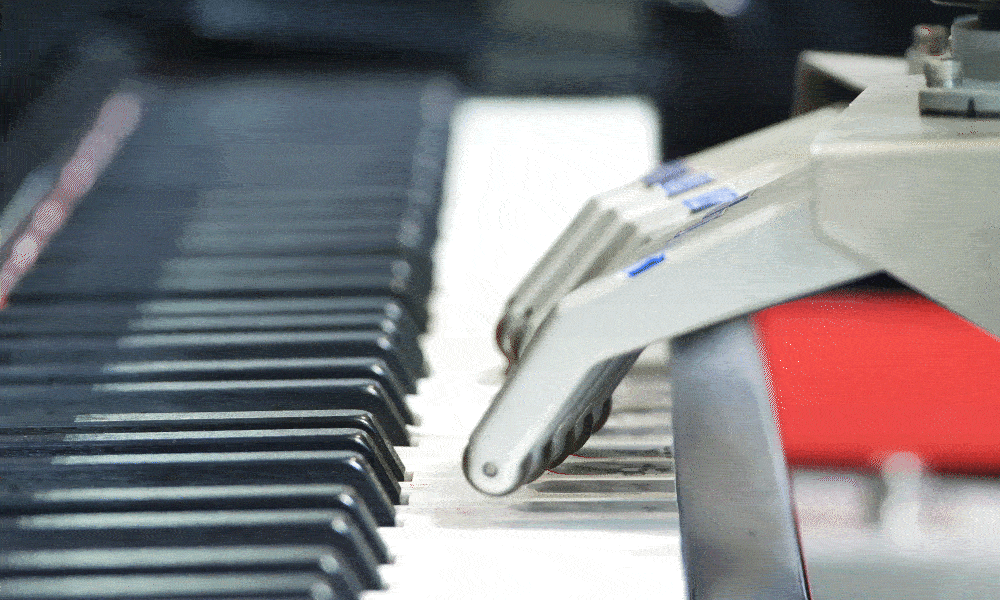 moving image of robotic hands playing on piano keyboard.