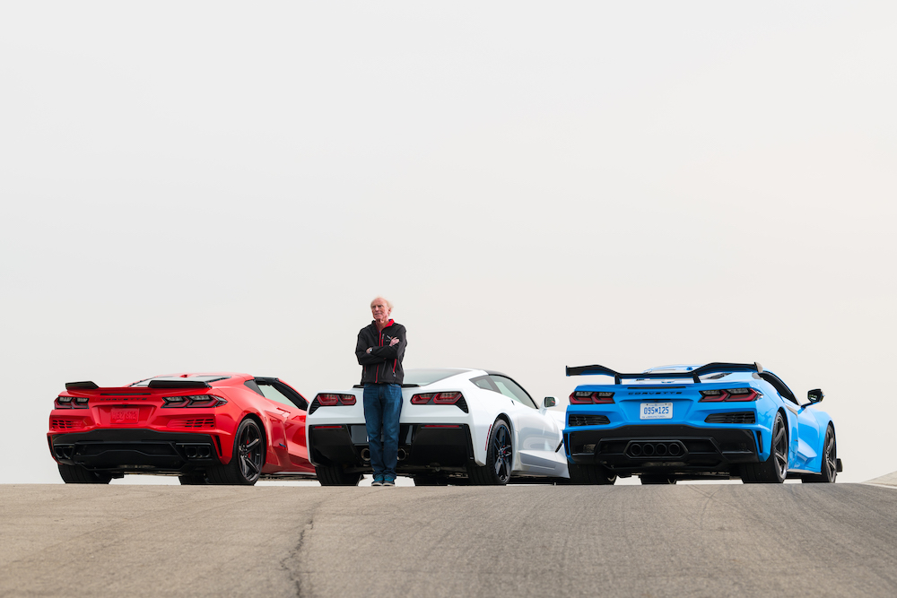 Man stands, with arms crossed, in front of red, white, and blue Corvettes