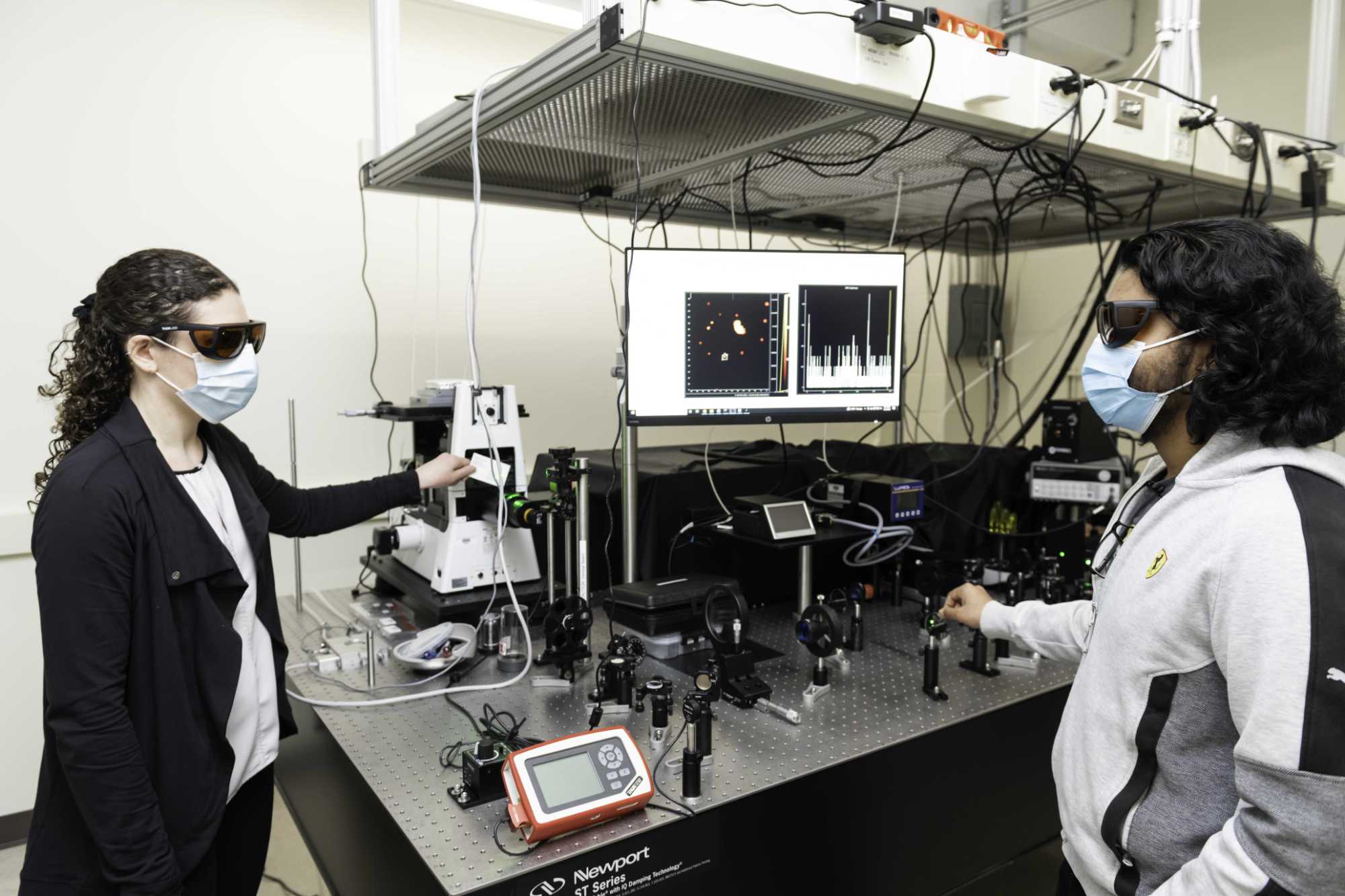 Andrea Pickel and Dinesh Bommidi in masks and protective eye gear near a laser system.