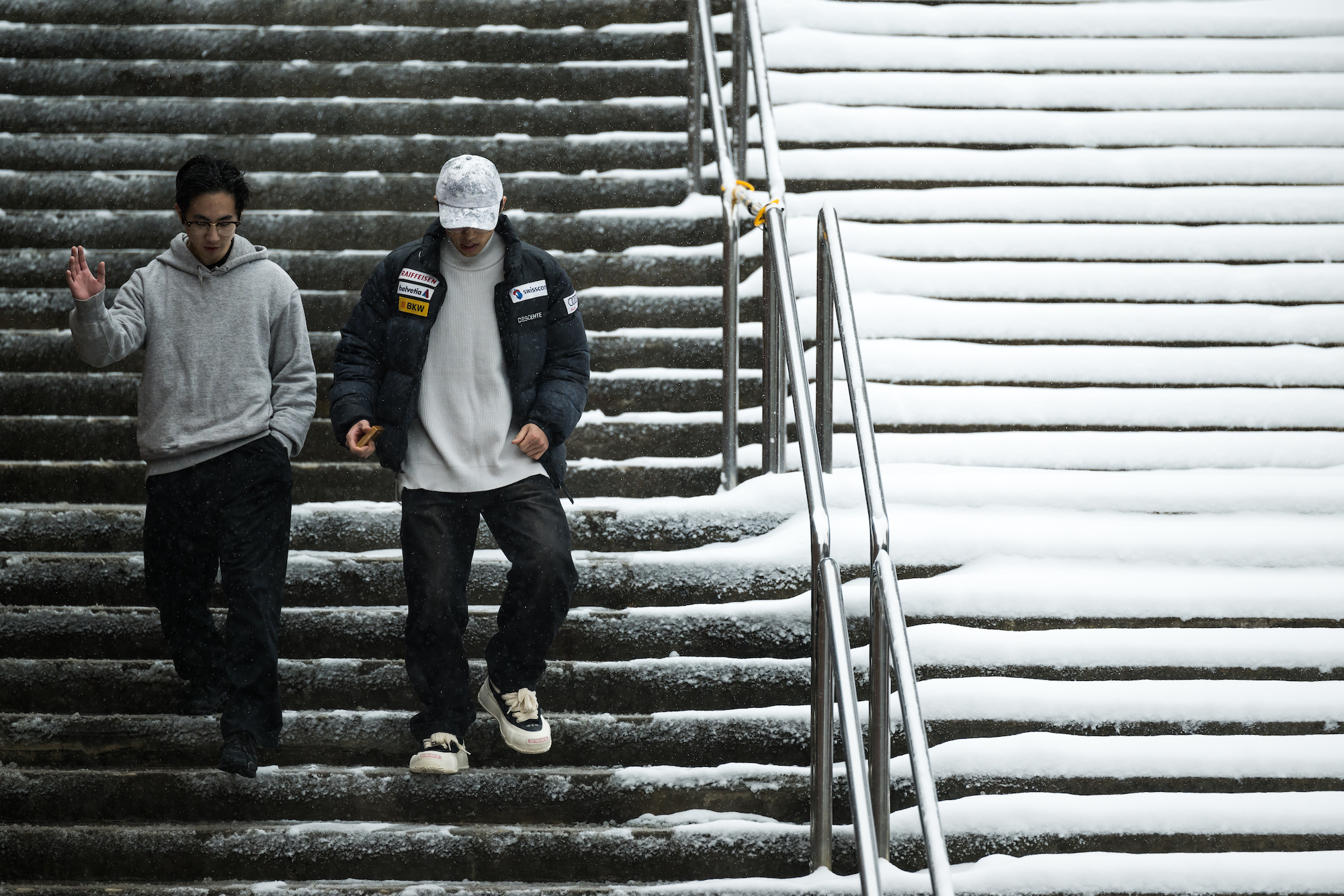 Two students in outerwear walk down snow-covered steps