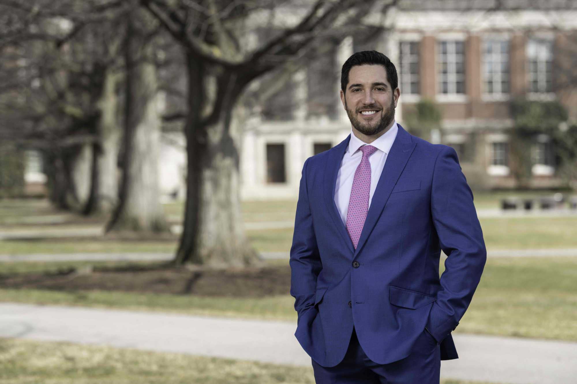 Robert Alexander in a suit smiles at the camera while on the Eastman Quadrangle. 