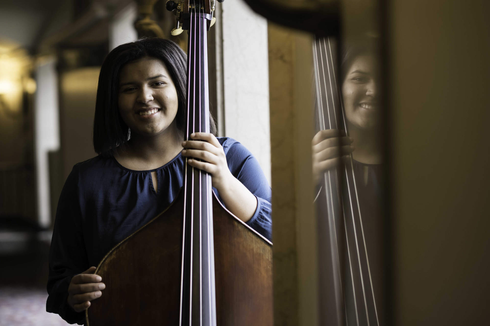 First-generation student Janae Gaddy smiles at the camera while posing with her double bass at the Eastman School of Music.