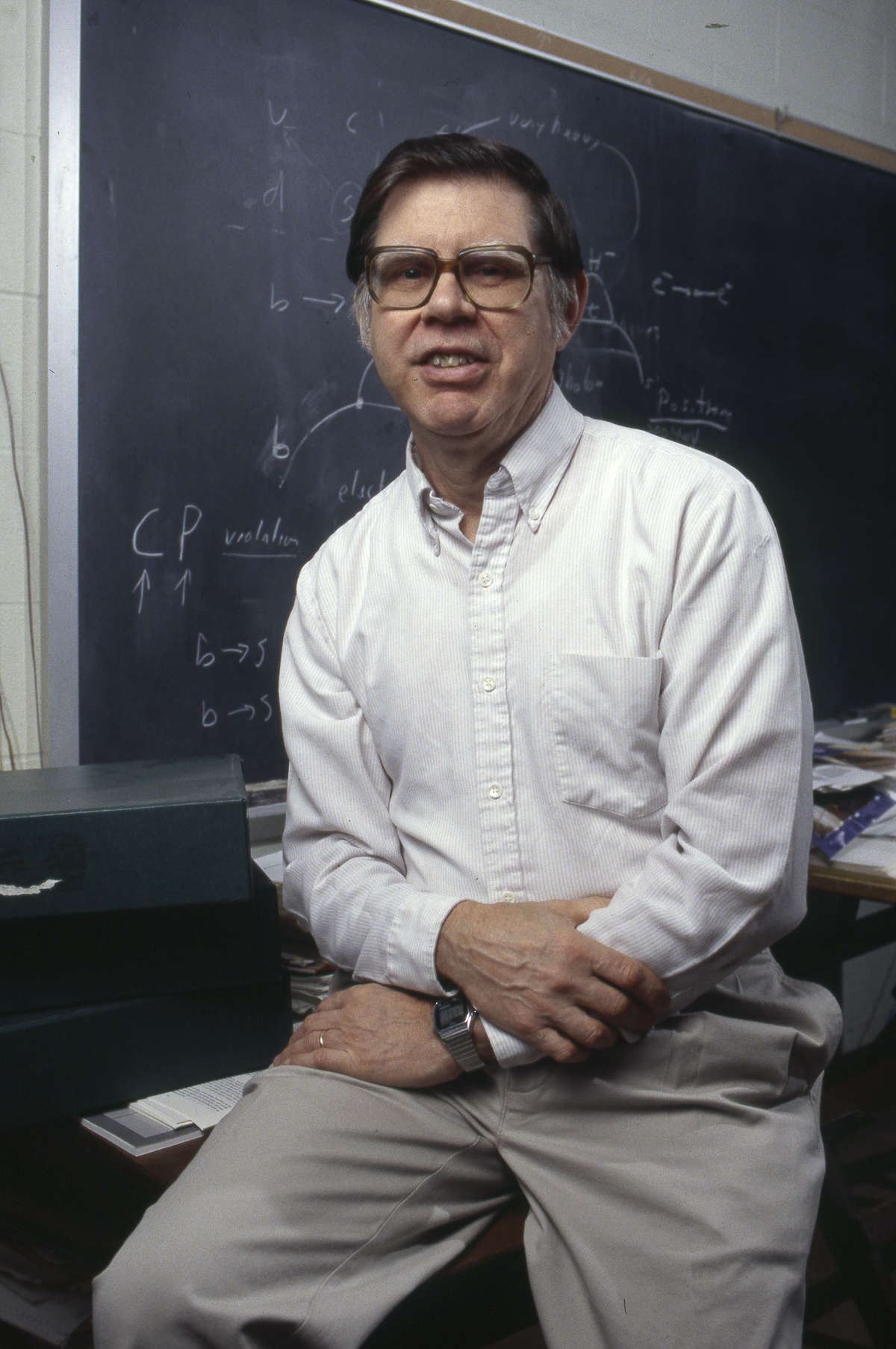 Edward Thorndike seated at the edge of a desk and smiling at the camera with a blackboard full of equations in the background.
