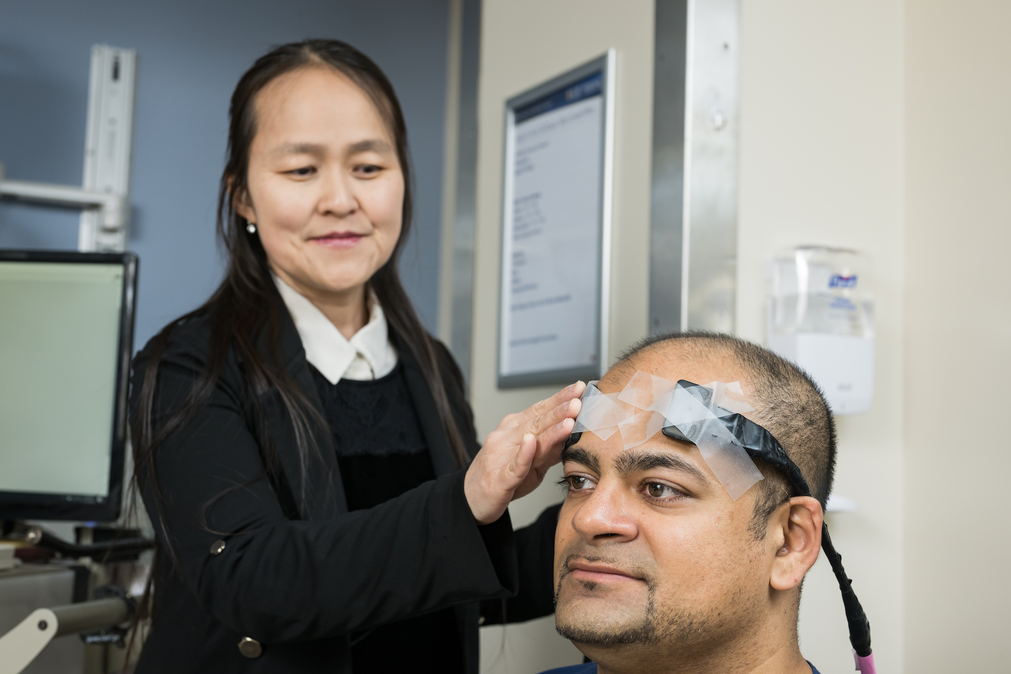 Male researcher models neuro-monitoring device as female researcher affixes device to his head