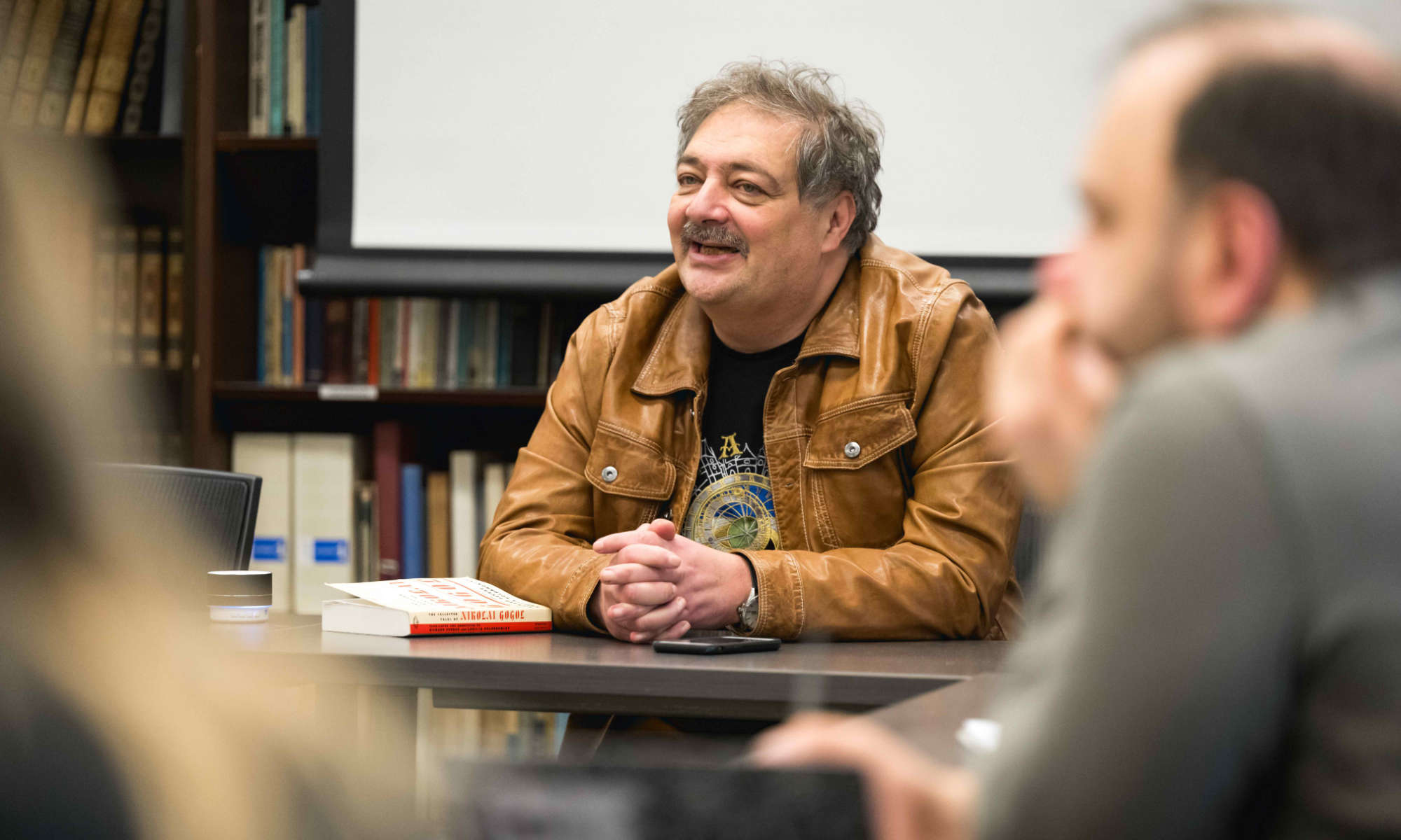 Dmitry Bykov seated at the front of a classroom with students in the foreground out of focus.