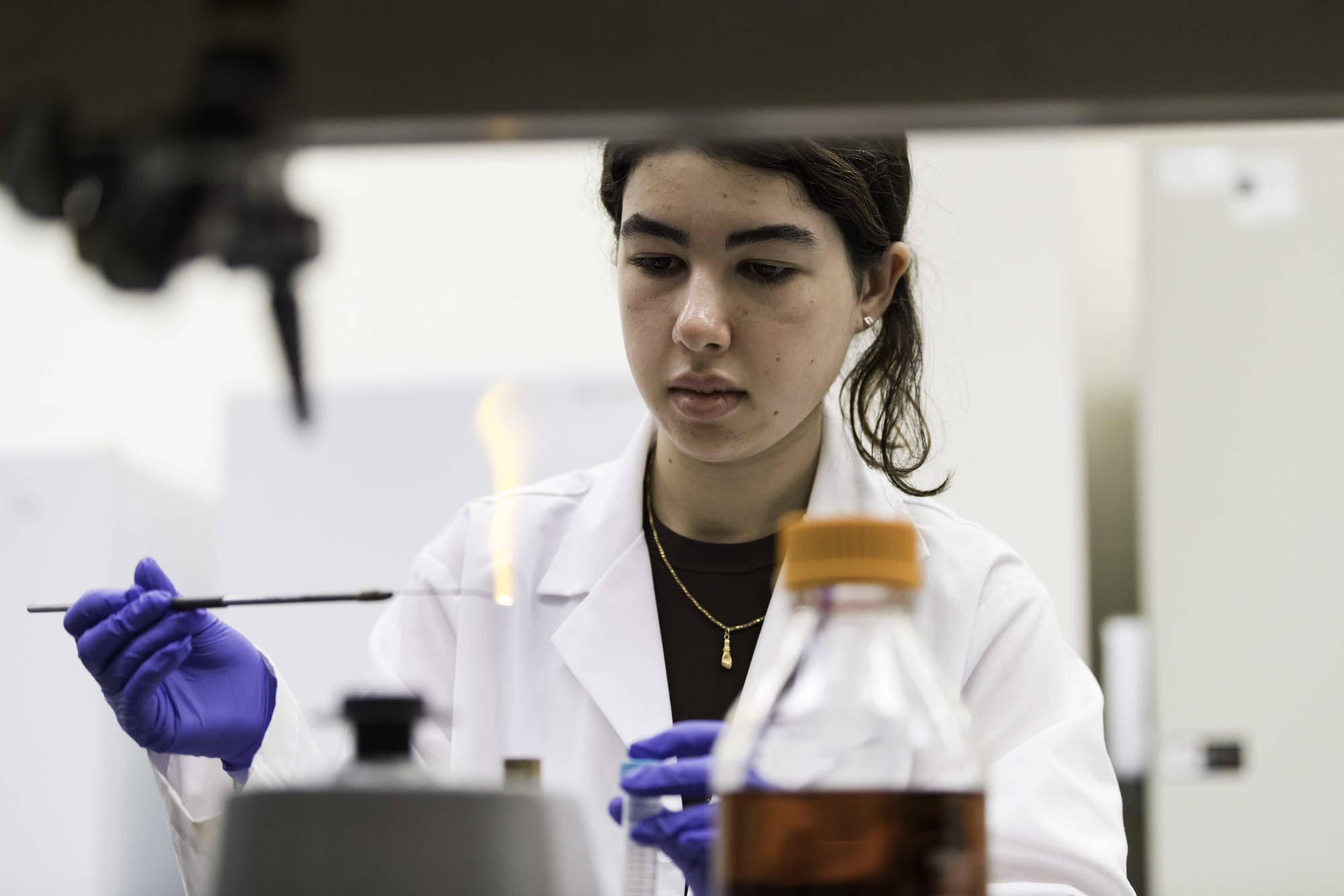 Student in a lab coat sterilizing an inoculation loop using a flame.