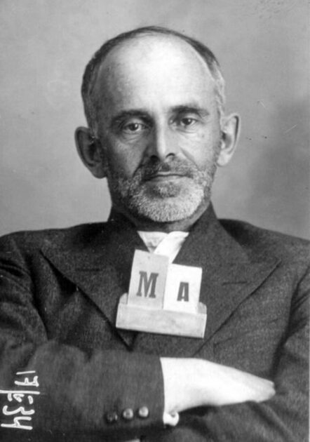 Black and white image of Russian poet Osip Mandelstam looking at the camera with his arms crossed.