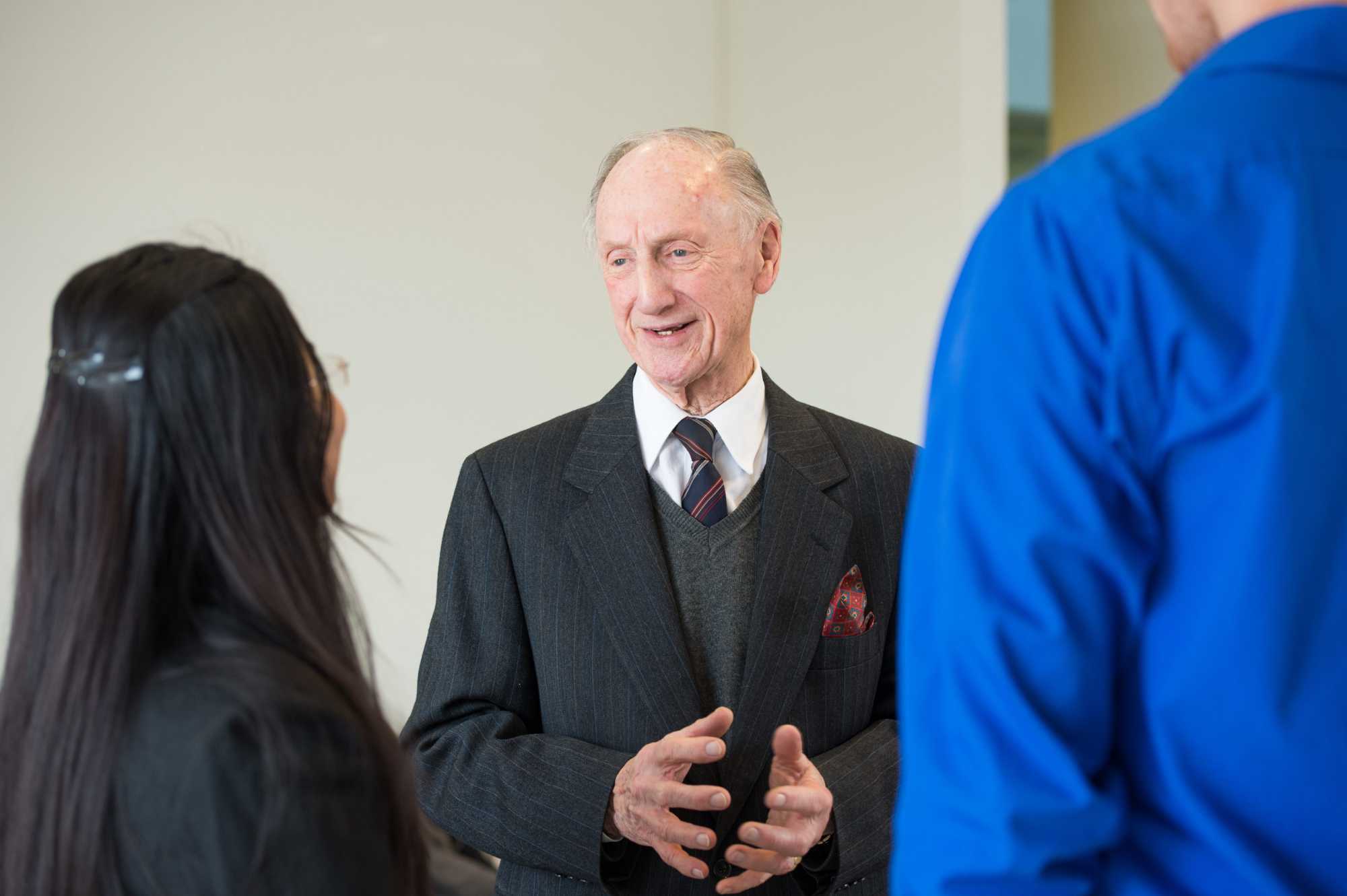 Brian J. Thompson in a suit speaking two two people seen from behind.