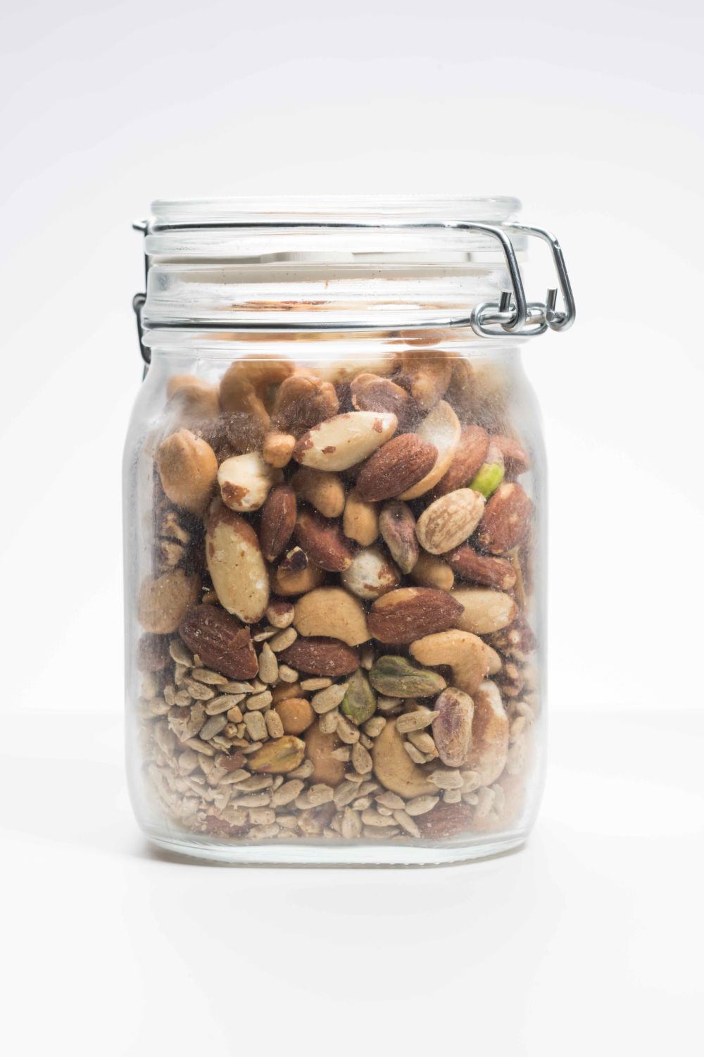 Clear clamp lid jar containing various-sized nuts with the bigger ones at the top and the smaller ones at the bottom to illustrate the Brazil Nut Effect, which occurs in granular systems.