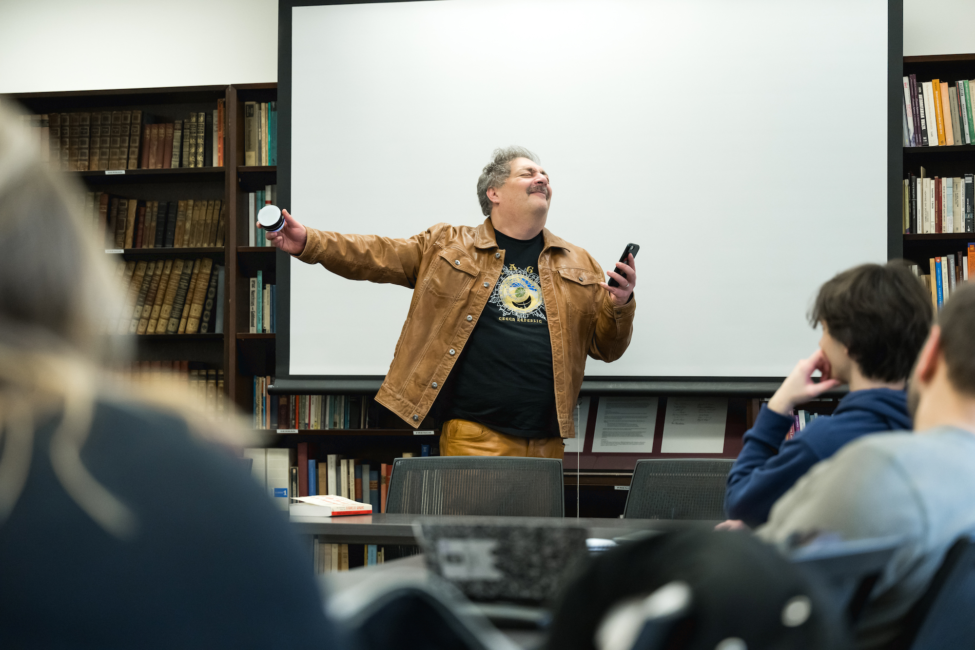 Professor holds a cell phone and a small speaker out in the direction of his students