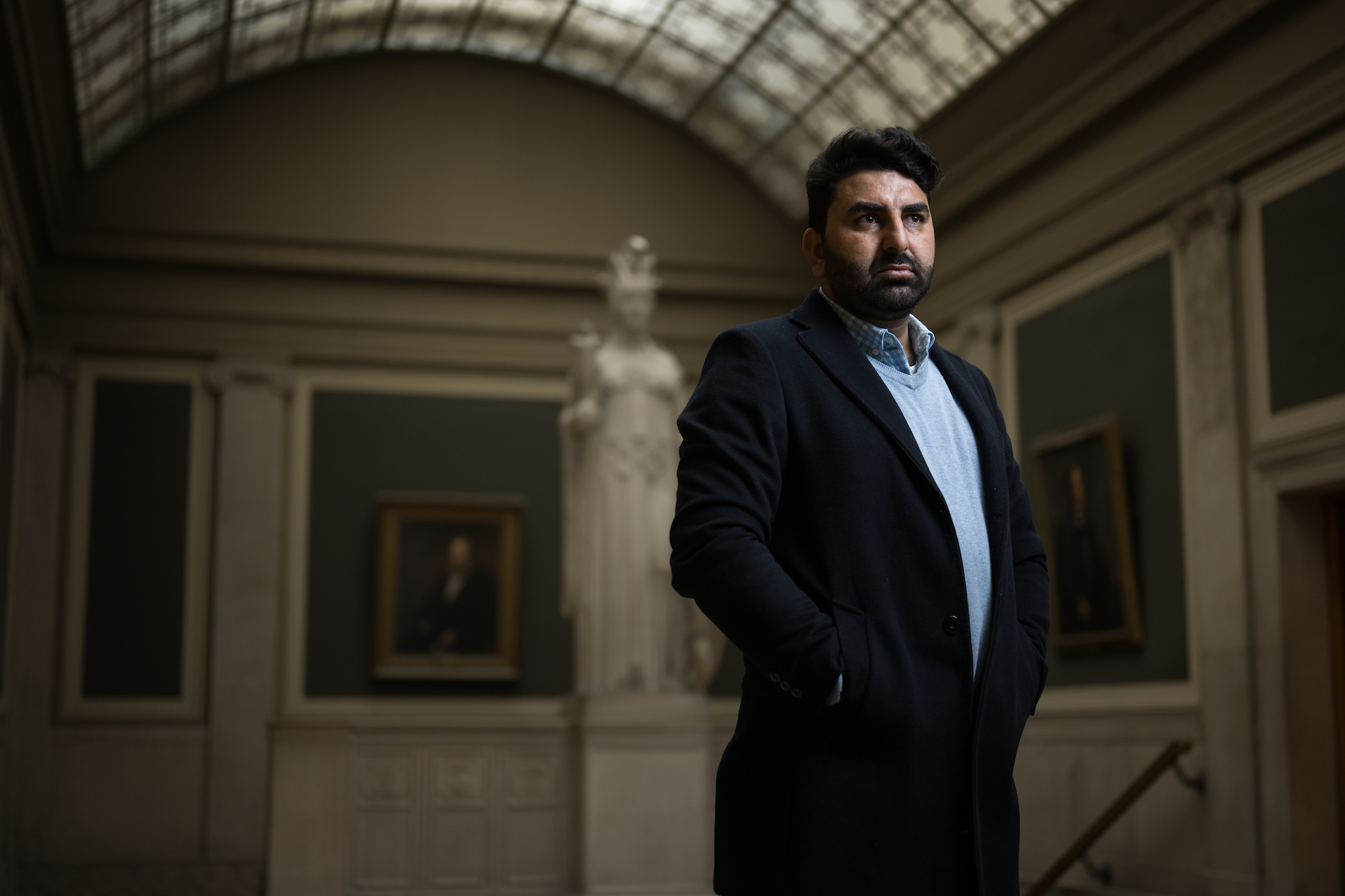 Profile of a man in an overcoat standing in the great hall of a library