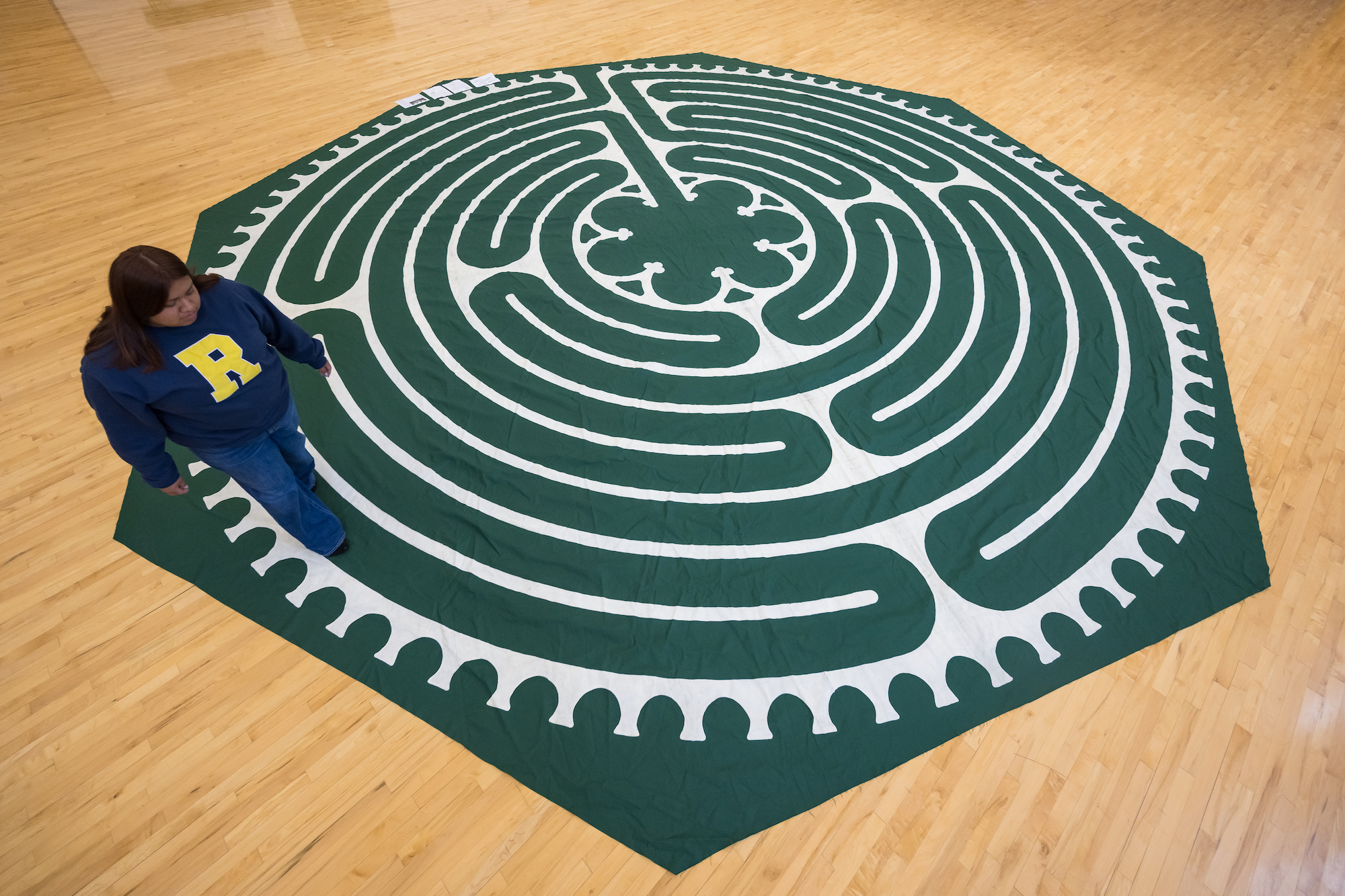 Student follows along a green and while floor labyrinth 