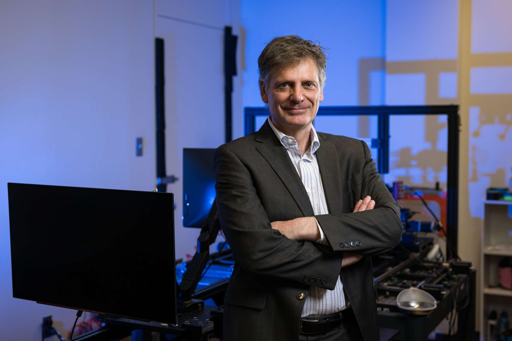 Michele Rucci with his arms crossed, smiling at the camera, while in his lab surrounded by eye tracking equipment. 