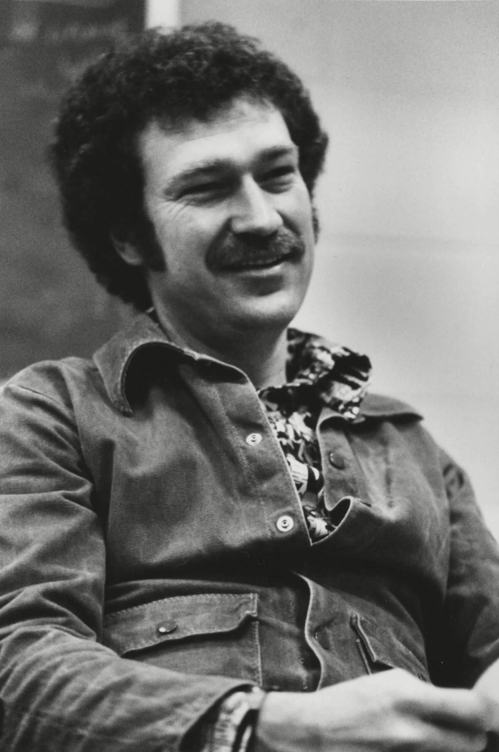 Black and white archival photo of Michael Jensen seated and leaning back dressed in a casual outfit.